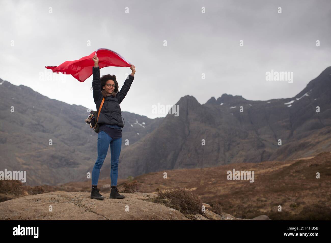 Donna che mantiene bandiera rossa in montagna, Fairy Piscine, Isola di Skye, Ebridi, Scozia Foto Stock