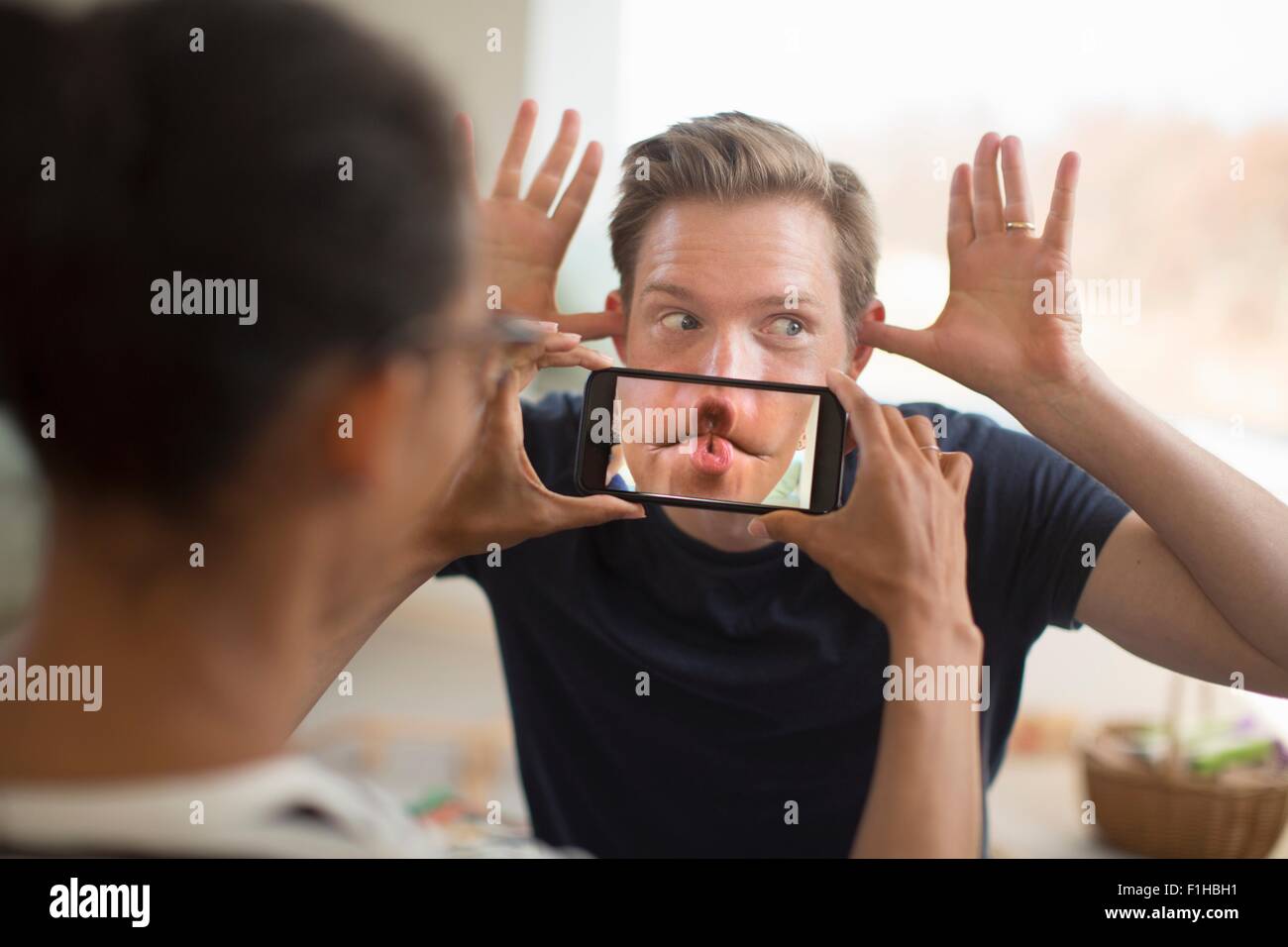 La donna lo smartphone di contenimento nella parte anteriore del la bocca dell'uomo, Foto Stock