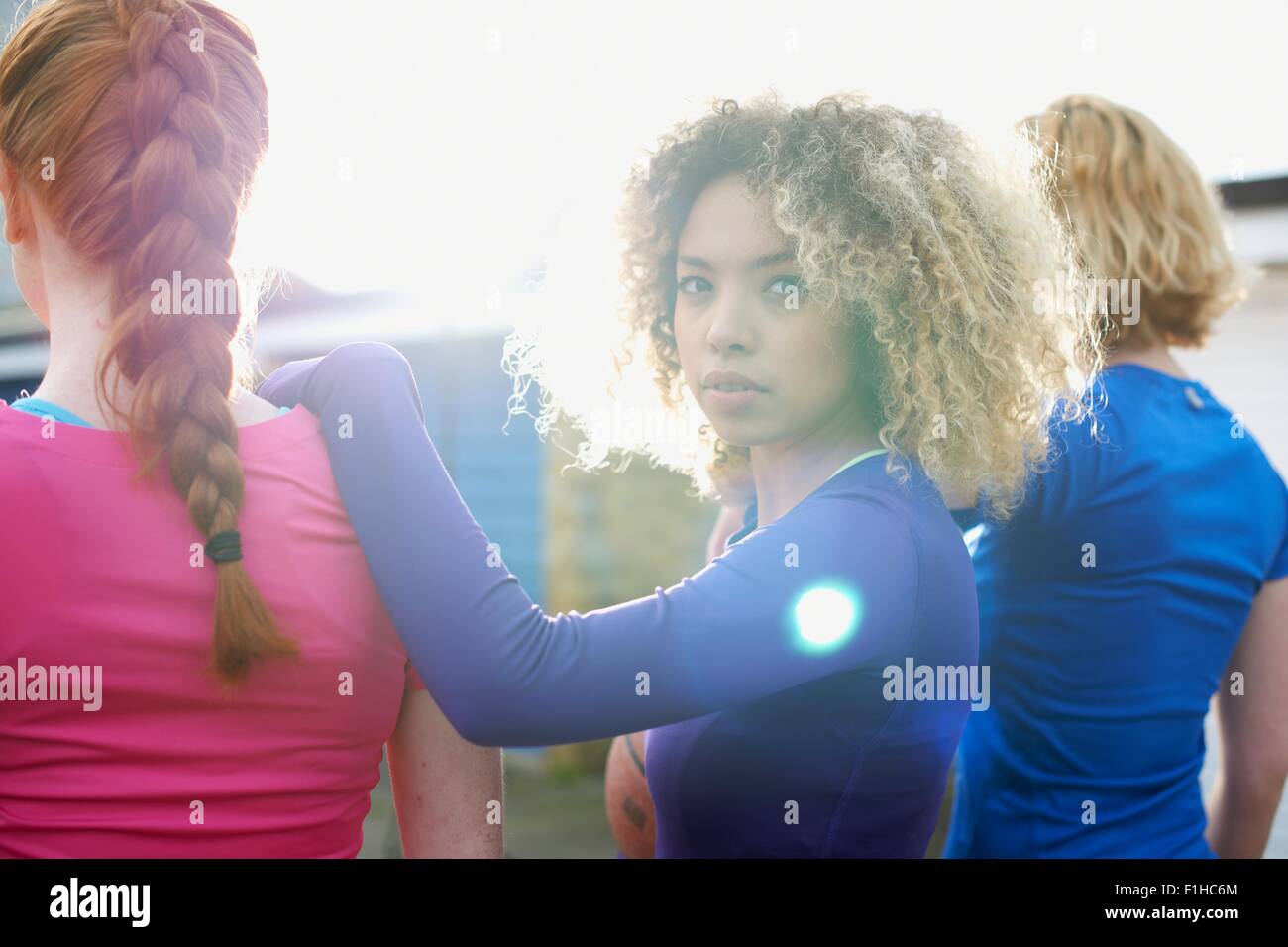 Vista posteriore di tre donne che esercitano insieme con una donna che guarda la fotocamera Foto Stock