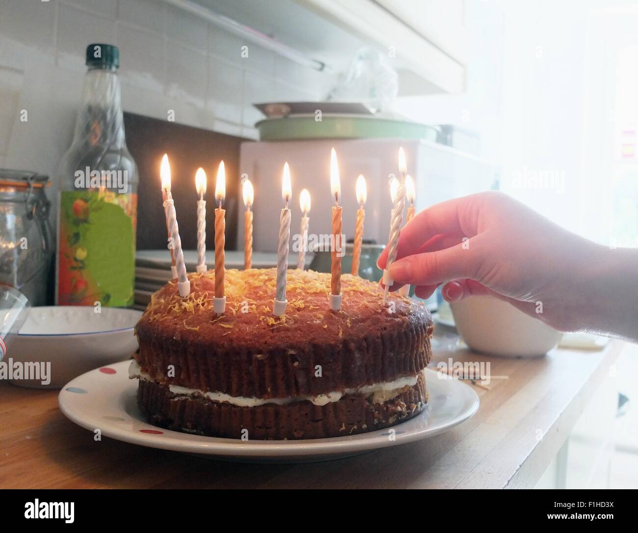 Mano di giovane donna mettendo candele accese sulla torta di compleanno Foto Stock