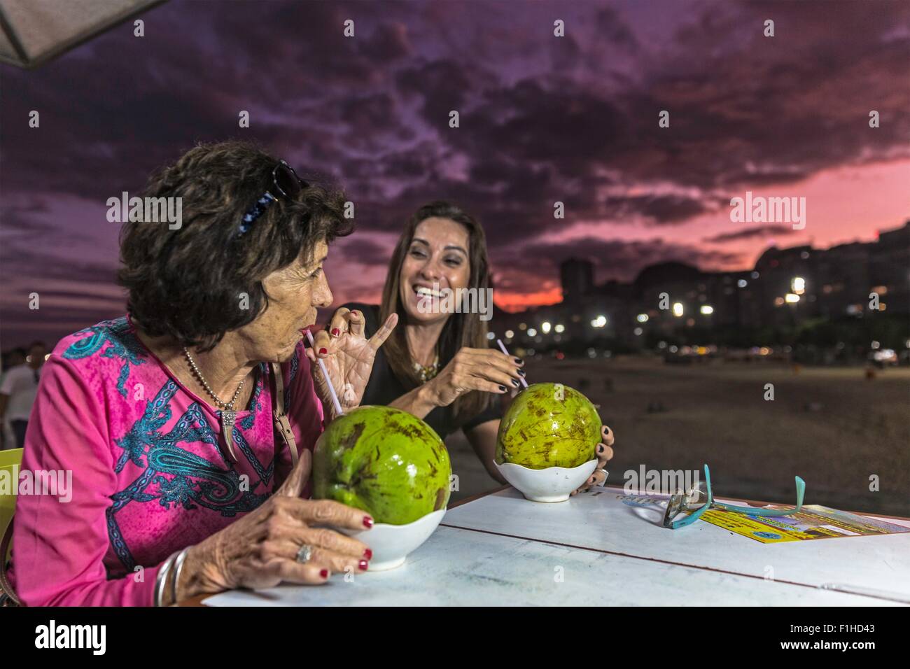 Donna matura e madre di bere da gusci di noce di cocco in spiaggia di notte, Copacabana, Rio de Janeiro, Brasile Foto Stock