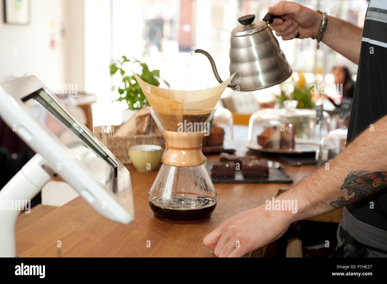 Le mani del cafe cameriere versando acqua bollente nel filtro del POT del caffè Foto Stock