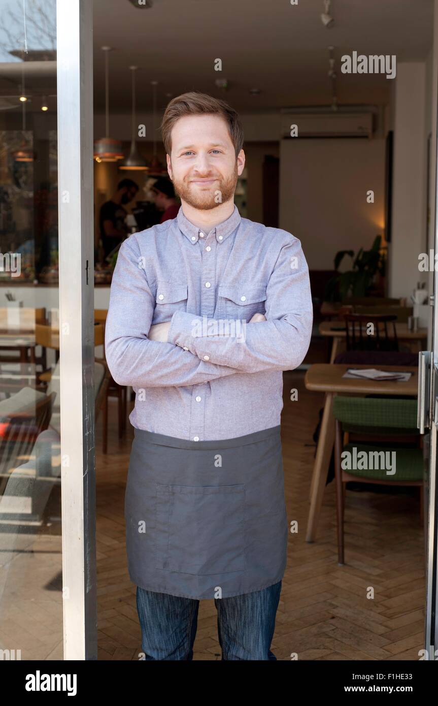 Ritratto di orgoglioso giovane maschio cafe proprietario nella porta Foto Stock