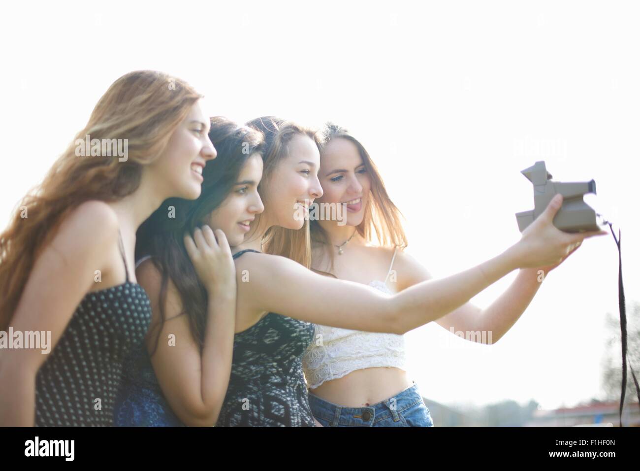 Quattro ragazze adolescenti tenendo la fotocamera istantanea selfie in posizione di parcheggio Foto Stock