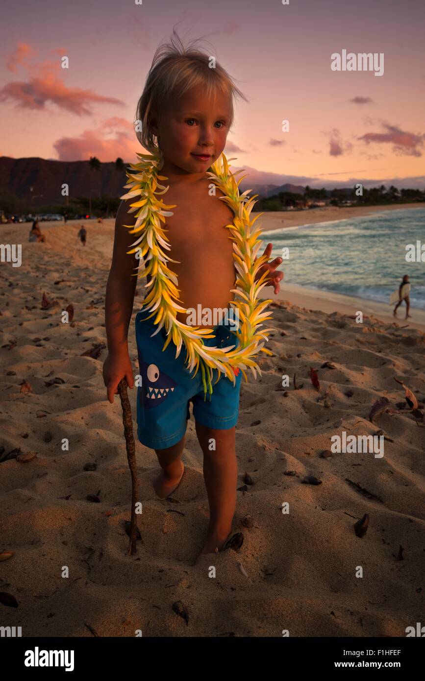 Giovane ragazzo indossa hawaiian garland, passeggiate lungo la spiaggia, Makaha, Oahu Island, Hawaii Foto Stock