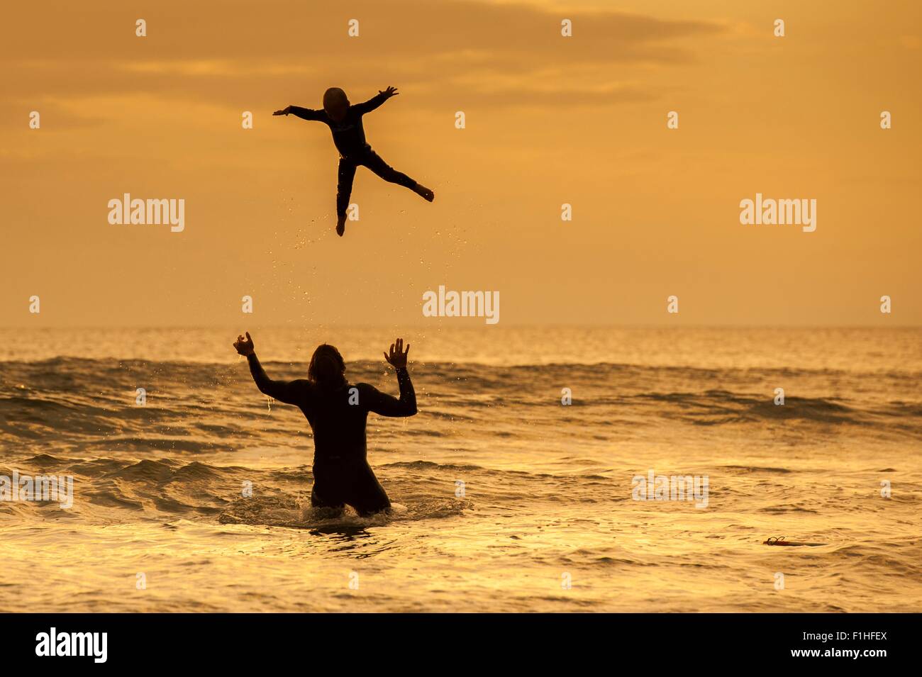 Padre figlio di lancio in aria, in mare al tramonto, Lahinch, Clare, Irlanda Foto Stock
