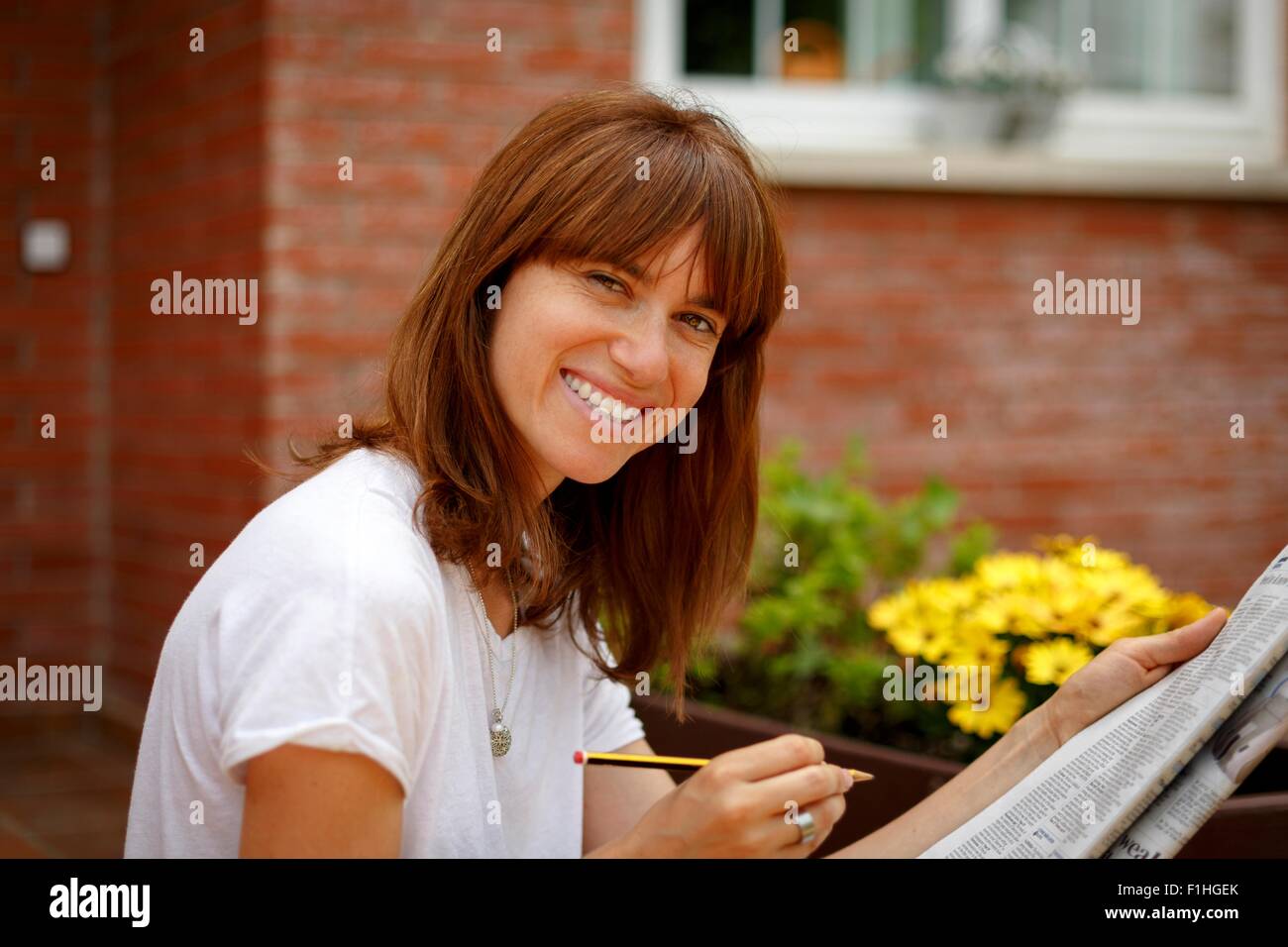 Metà donna adulta seduti all'aperto facendo il cruciverba, guardando la telecamera, sorridente Foto Stock