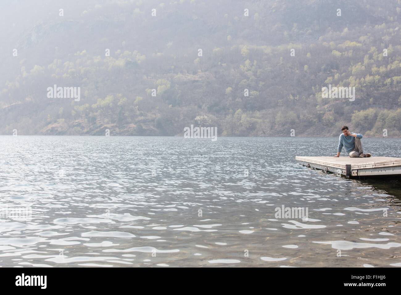 Giovane uomo chattare su smartphone sul molo, Lago di Mergozzo, Provincia di Verbania, Piemonte, Italia Foto Stock