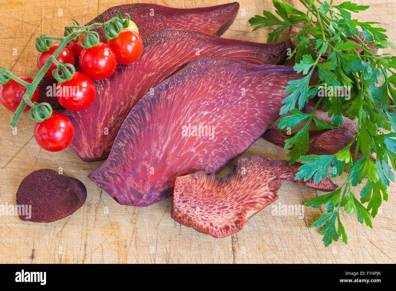 La sezione da Fistulina hepatica (bistecca di manzo fungo) e pomodorini e foglie di prezzemolo su sfondo di legno Foto Stock