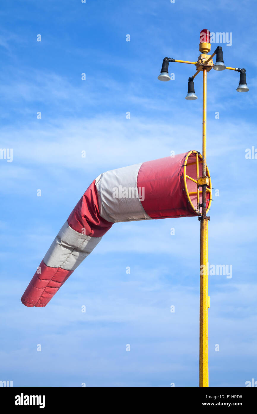 Indicatore del vento come un aeroporto attrezzatura. Rosso e bianco striato indicatore del vento su blu cielo nuvoloso Foto Stock