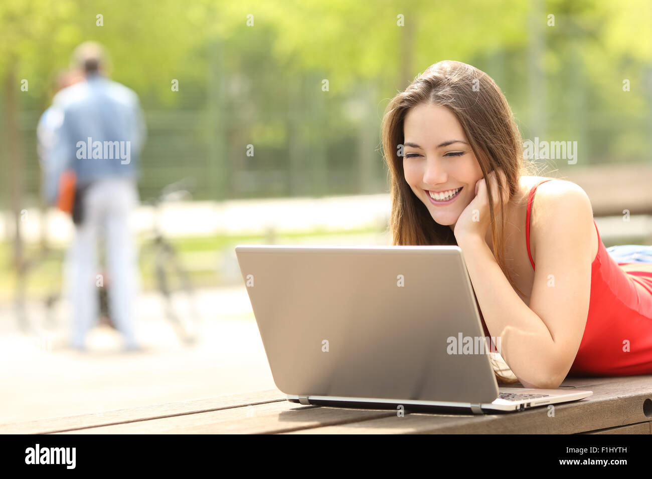 Felice adolescente studente ragazza utilizzando un computer portatile in un campus o park giacente su un banco di lavoro Foto Stock