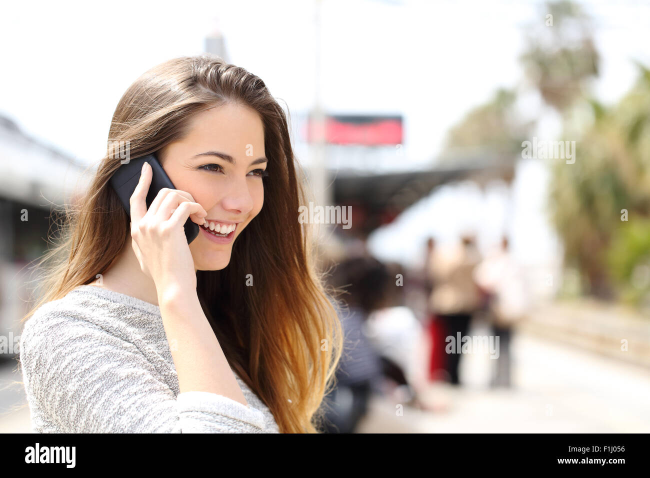 Donna che parla al telefono tenendo una conversazione mentre si è in attesa in una stazione ferroviaria Foto Stock