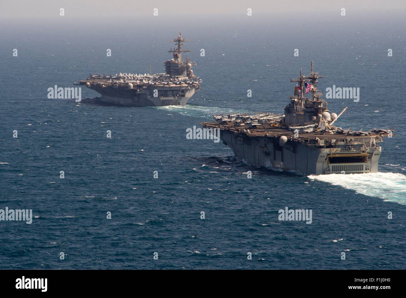 Stati Uniti Nimitz Navy-class portaerei nucleare USS Theodore Roosevelt transita lungo il Wasp-classe assalto anfibio nave USS Essex durante il funzionamento inerenti risolvere combattendo lo Stato islamico Agosto 29, 2015 nel Mare Arabico. Foto Stock