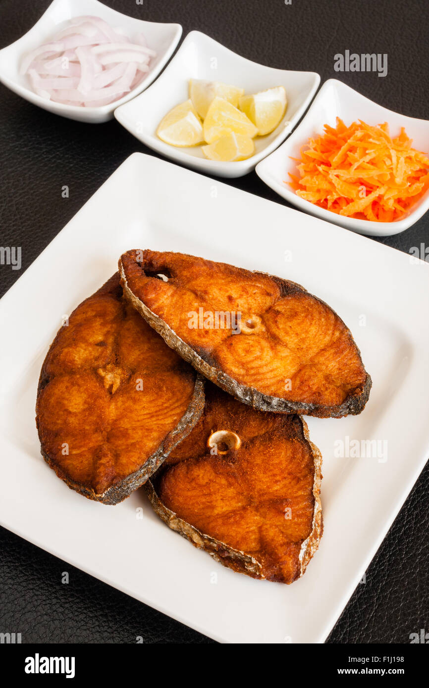Primo piano della deliziosa seer/sgombro filetti di pesce fritto servito con le carote grattugiate, materie anelli di cipolla, limone. Foto Stock