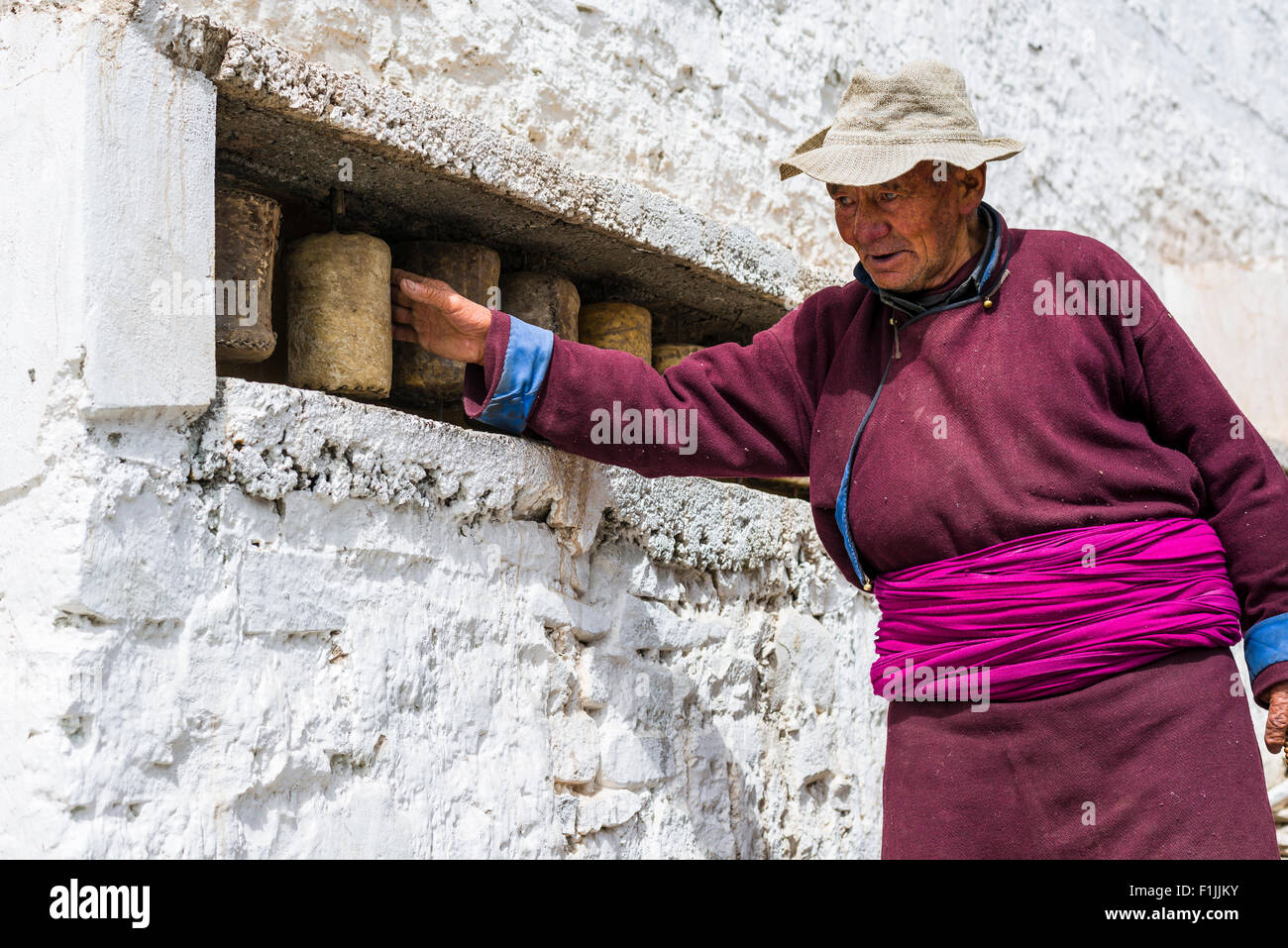 Un vecchio uomo Ladakhi sta girando in una preghiera della ruota in corrispondenza di una parete di Hemis Gompa, Hemis, Jammu e Kashmir India Foto Stock