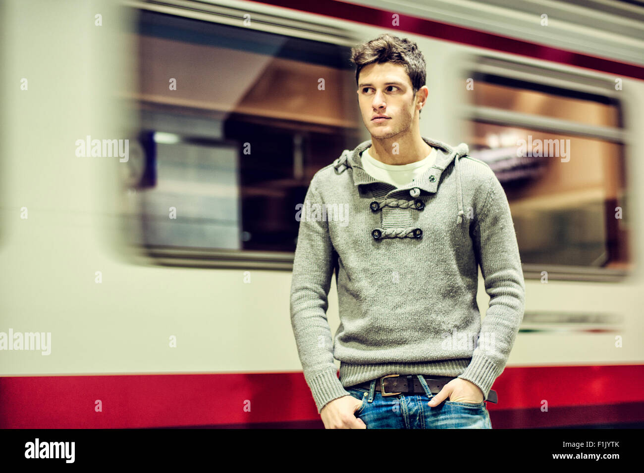 Bel giovane all'interno della stazione ferroviaria che guarda lontano nella parte anteriore del treno in movimento carro Foto Stock