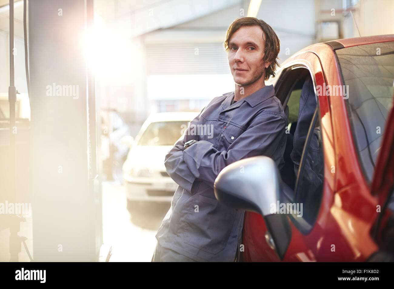 Ritratto fiducioso di inclinazione meccanico sulla vettura nel negozio di riparazioni auto Foto Stock