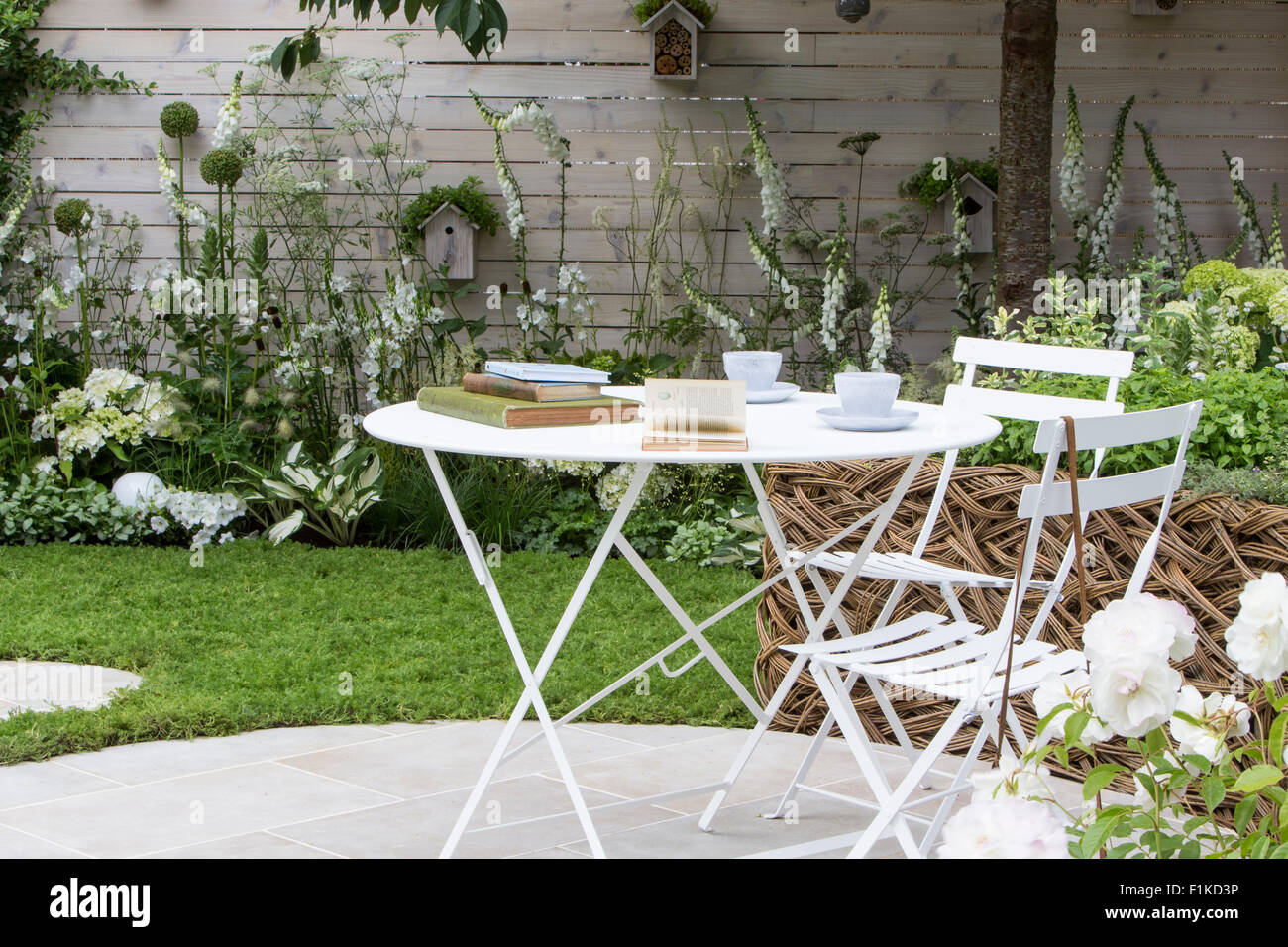 Patio circolare con tavolo e sedie, giardino piantato con piante di fiori bianchi in un bordo, recinzione bianca dipinta e scatole di uccelli Flower Show UK Foto Stock