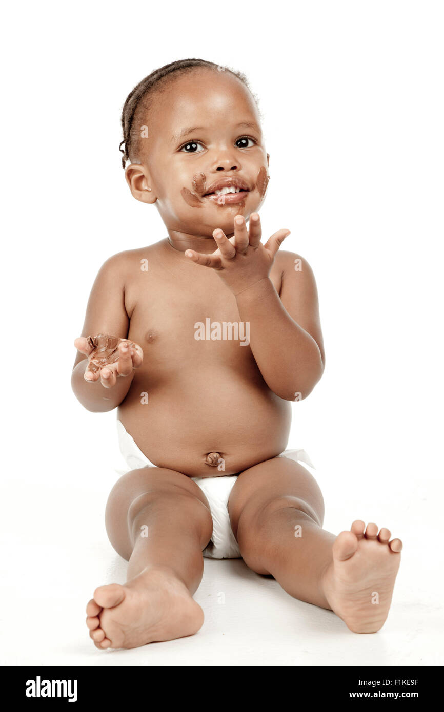 Un bambino si siede di fronte a uno sfondo bianco con il cioccolato in tutto il suo volto Foto Stock