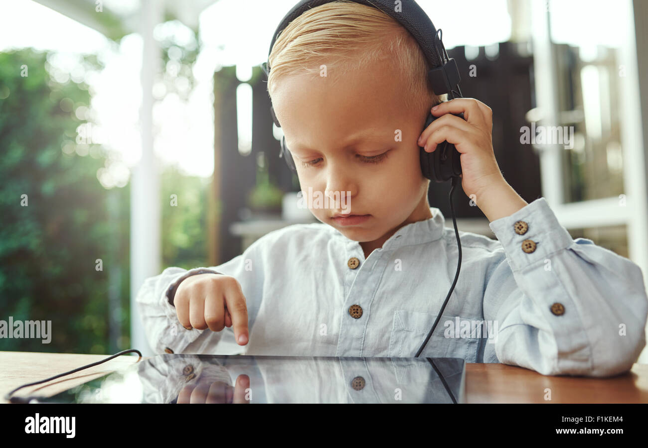 Little Boy ascoltando la sua musica selezionata colonna sonora che egli ha scelto di spegnere il touch screen sul suo computer tablet con il suo ey Foto Stock