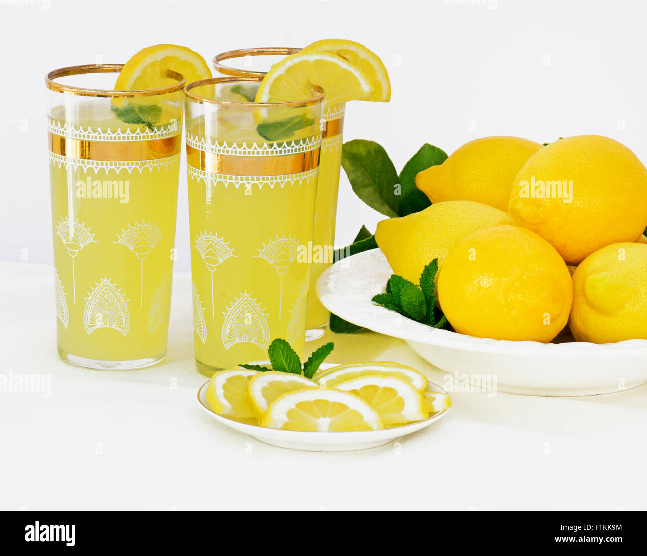 Bevande ghiacciate di limonata con la menta in bicchieri con rivestimento in oro e un piatto di appena raccolto i limoni a lato con il limone lea Foto Stock