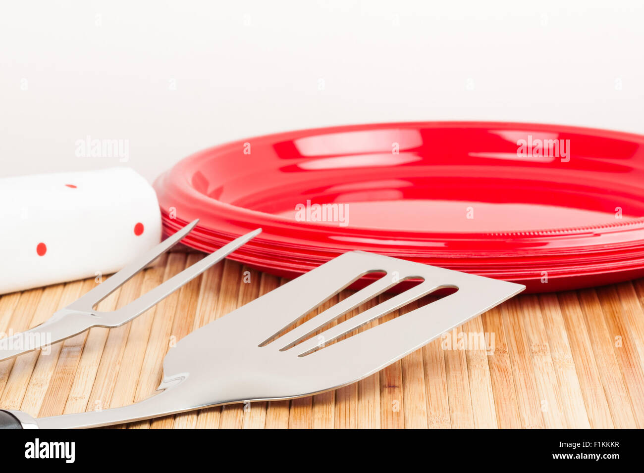 Un set di strumenti di barbecue e piastre di plastica su un tappetino di bambù simboleggia i barbecue tempo. Foto Stock