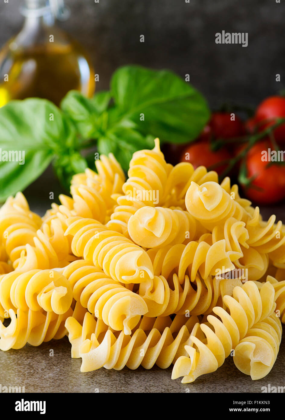 Fusilli non cotti fotografato con il fuoco selettivo nella finestra luce su un effetto di ardesia piastrella con basilico e pomodorini Foto Stock