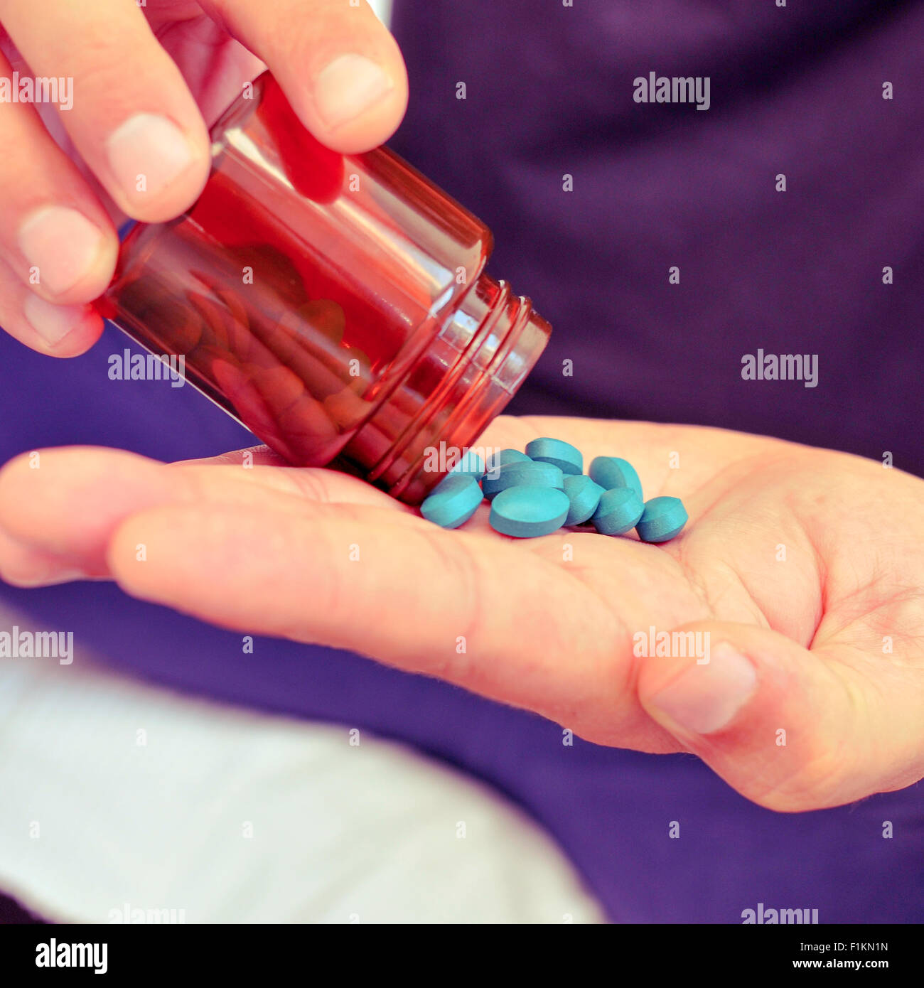 Primo piano di un giovane uomo caucasico con alcune pillole blu nella sua mano da una bottiglia Foto Stock