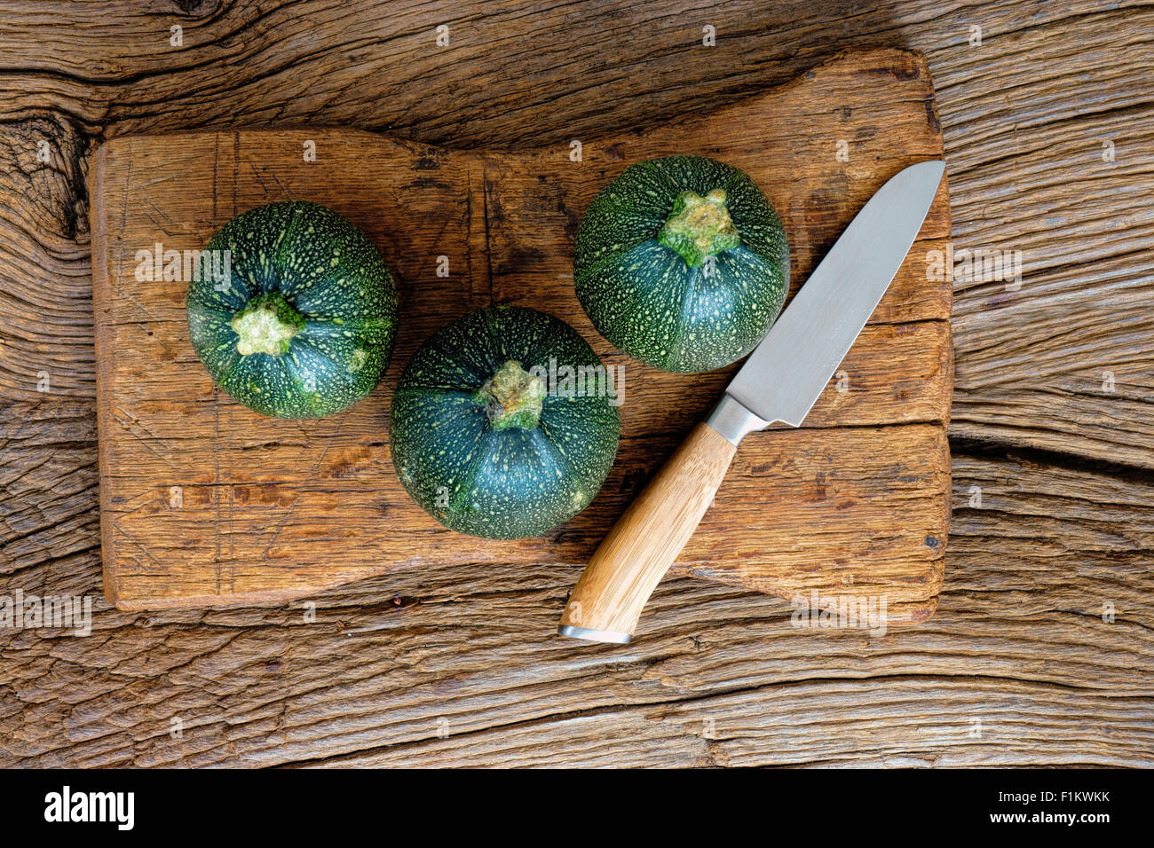 Tre round e mature, zucchine e un coltello da cucina rustica sul tagliere di legno Foto Stock