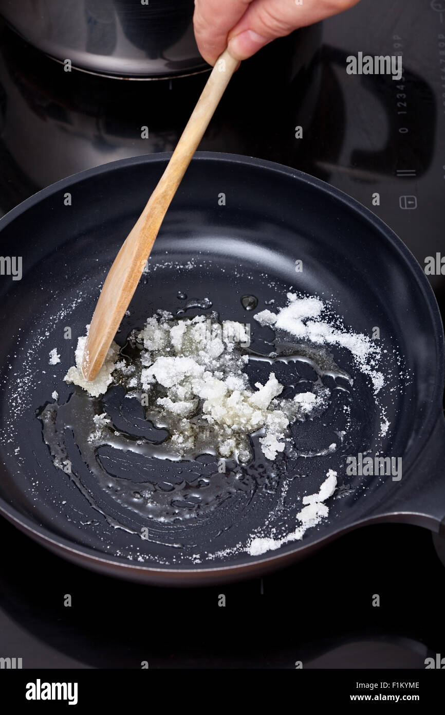 Mescolare lo zucchero con il cucchiaio di legno in una padella per caramellare Foto Stock