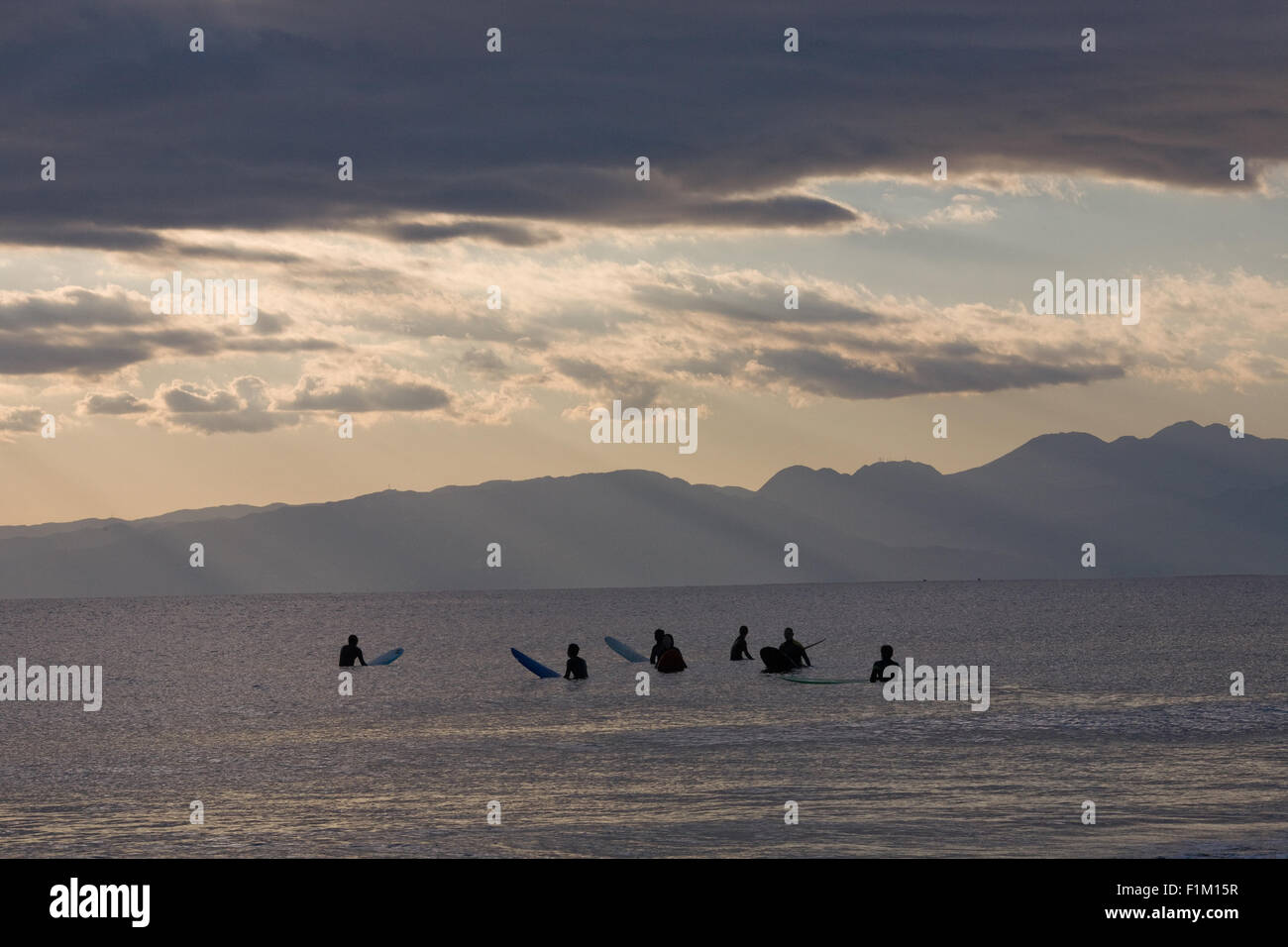 Gruppo di surfers seduti sulle loro tavole da surf in mare nuvole Foto Stock