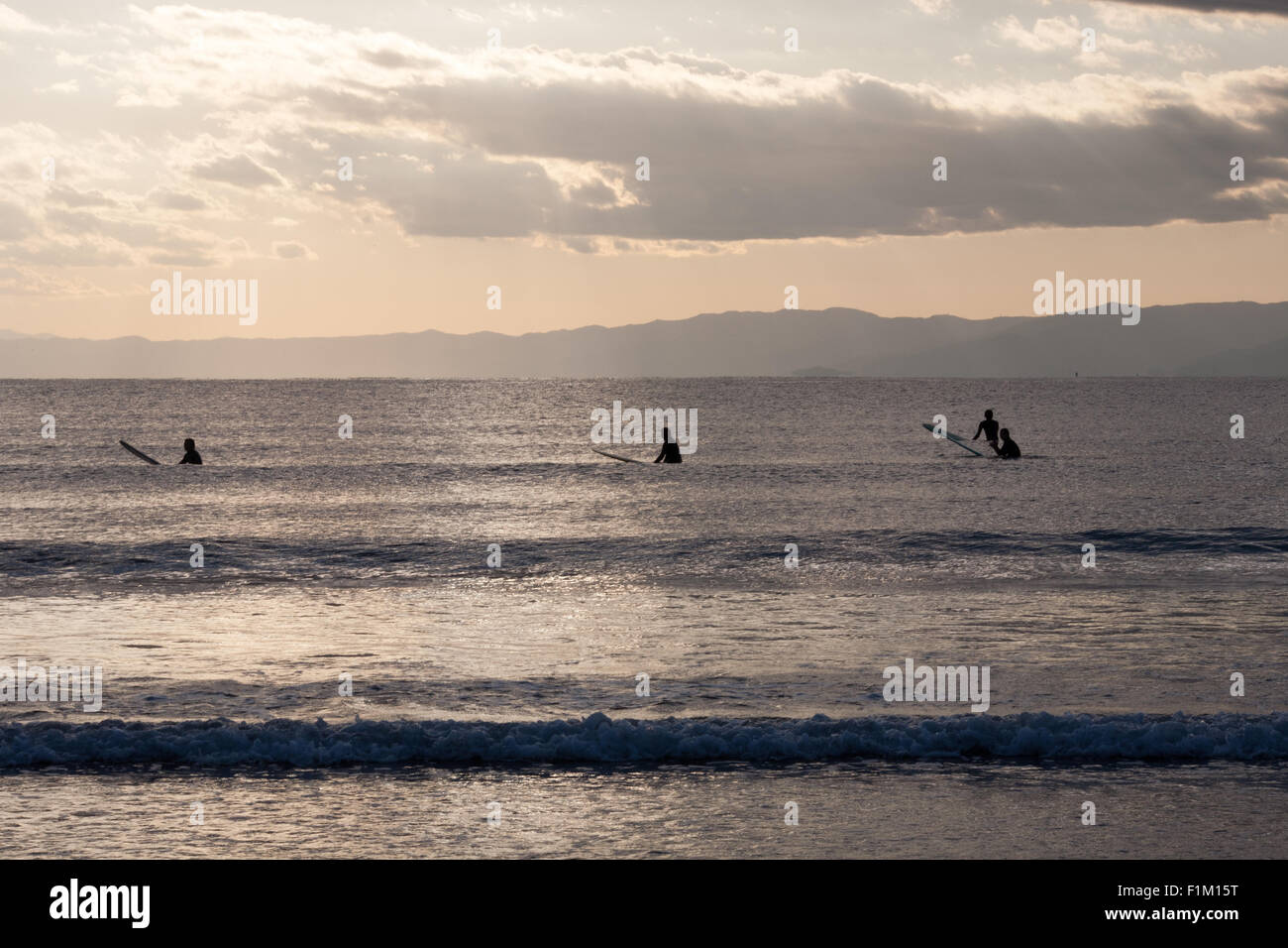 Quattro surfers seduti sulle loro tavole da surf in mare nuvole Foto Stock
