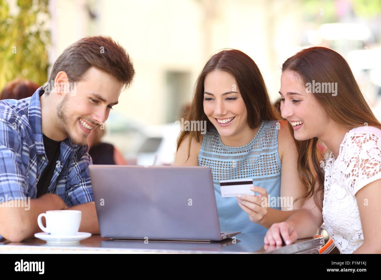 Tre amici felice shopping online con una carta di credito e un computer portatile in un coffee shop Foto Stock