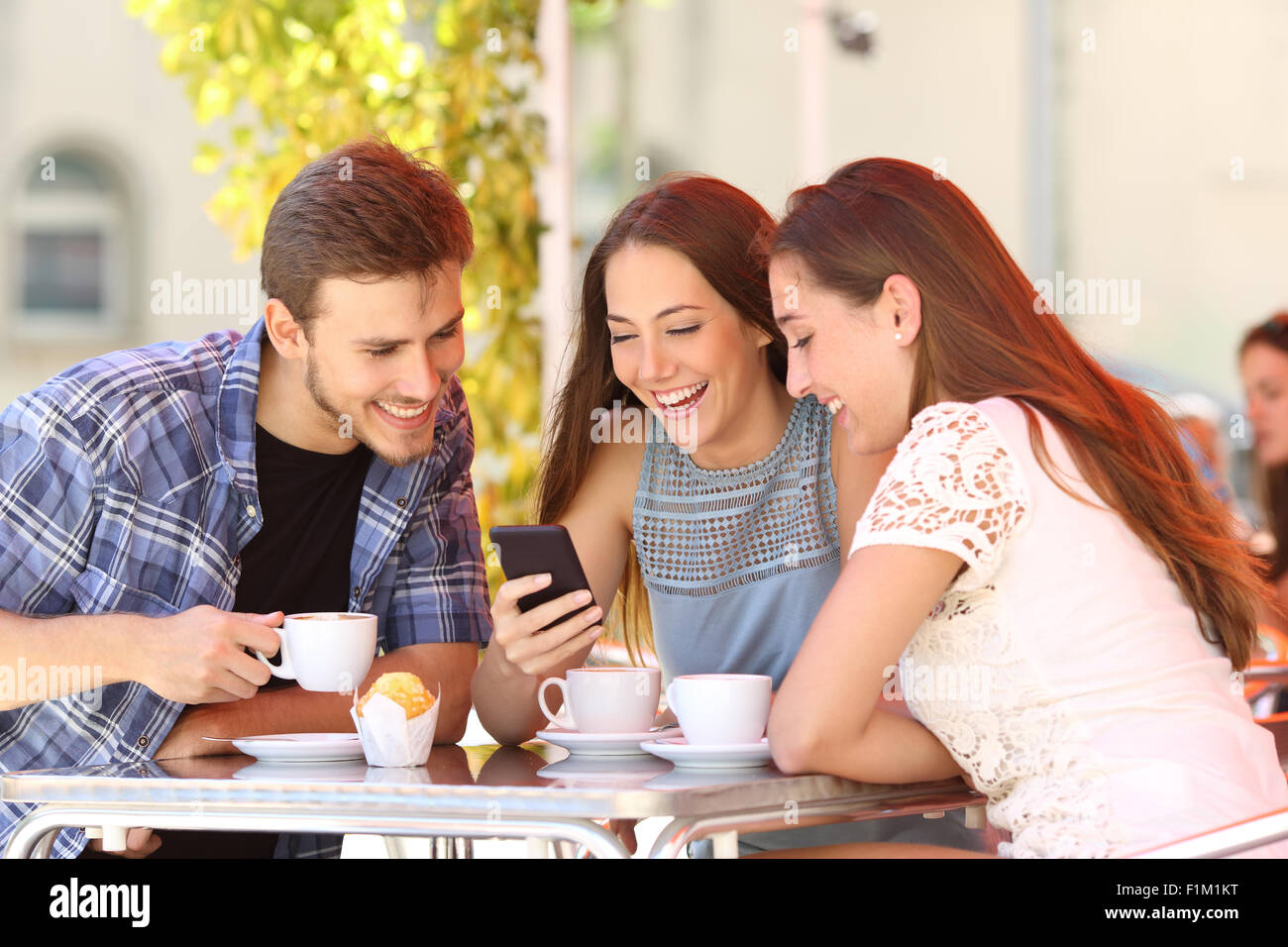 Tre amici felice guardando i social media in un telefono intelligente in un coffee shop Foto Stock