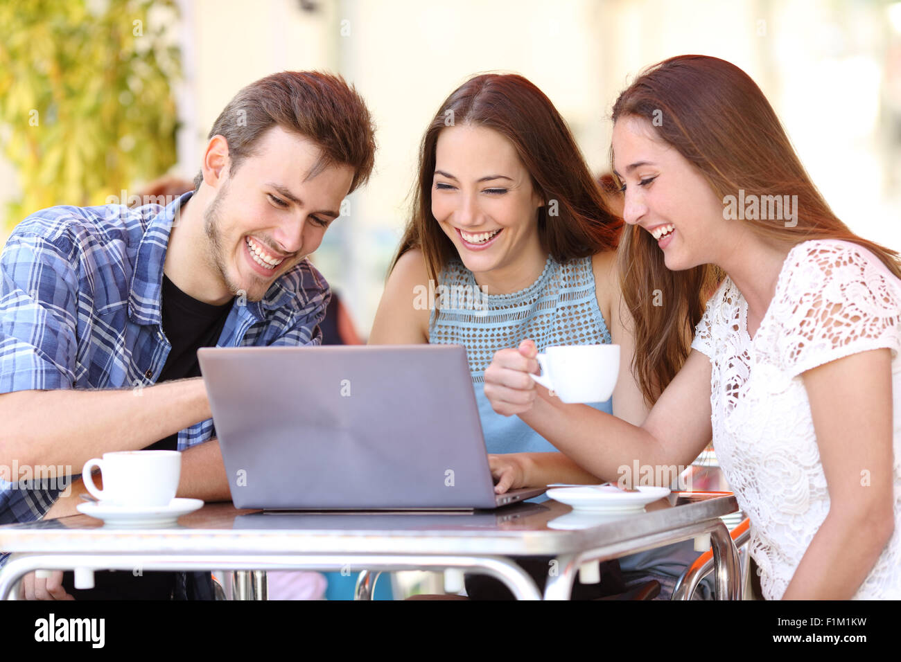Tre amici felici di guardare i video in un computer portatile in una caffetteria e terrazza Foto Stock