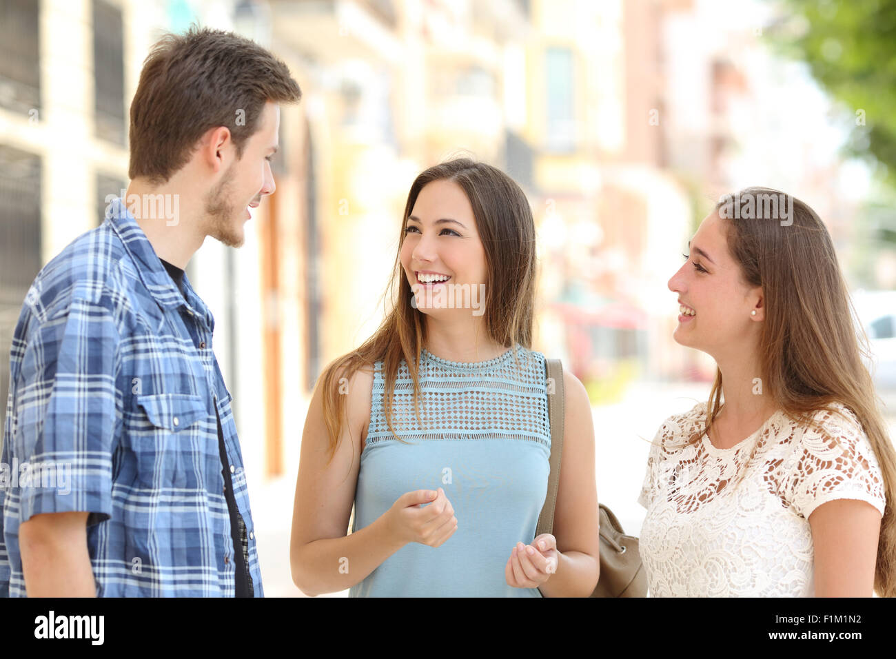 Tre amici felice di parlare tenendo una conversazione sulla strada in una giornata di sole con edifici in background Foto Stock