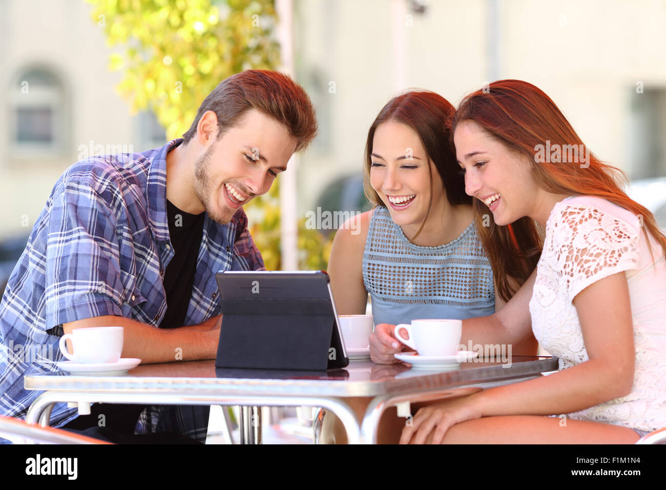 Tre amici felice guardando la tv o i social media in una compressa in una caffetteria e terrazza Foto Stock