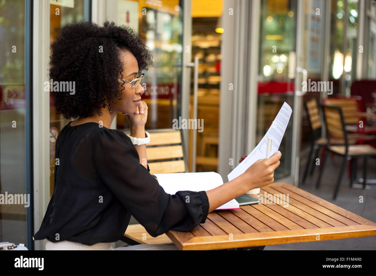 Giovane donna presso la caffetteria e la lettura di un documento Foto Stock