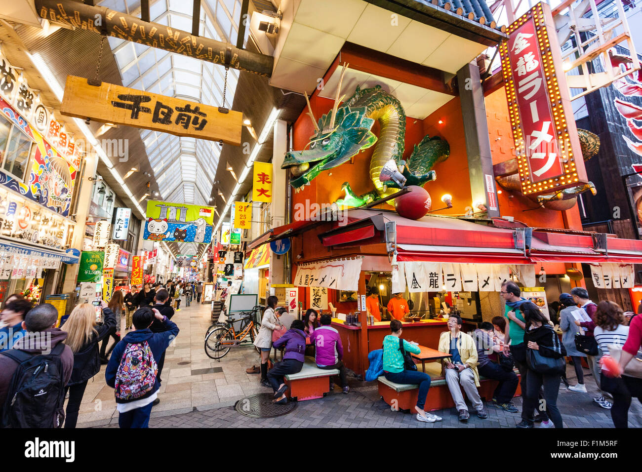 Giappone, Osaka. Dotonbori, famoso Kinryu Ramen noodle angolo ristorante con Golden Dragon figura segno sopra. La gente seduta fuori a cena a mangiare. Occupato. Foto Stock