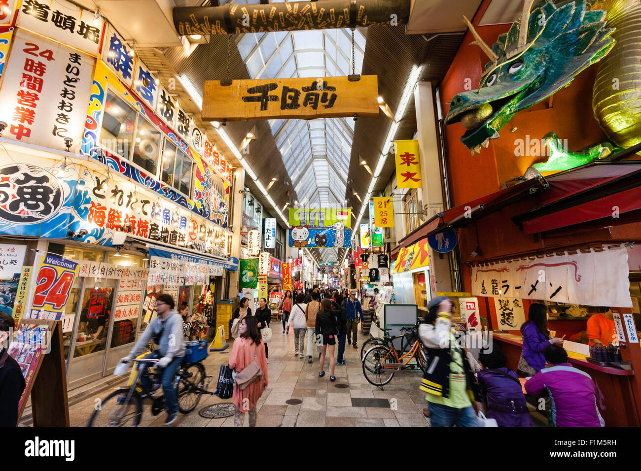Giappone, Osaka. Dotonbori, famoso Kinryu Ramen noodle angolo ristorante con Golden Dragon figura segno sopra. La gente seduta fuori a cena a mangiare. Occupato. Foto Stock