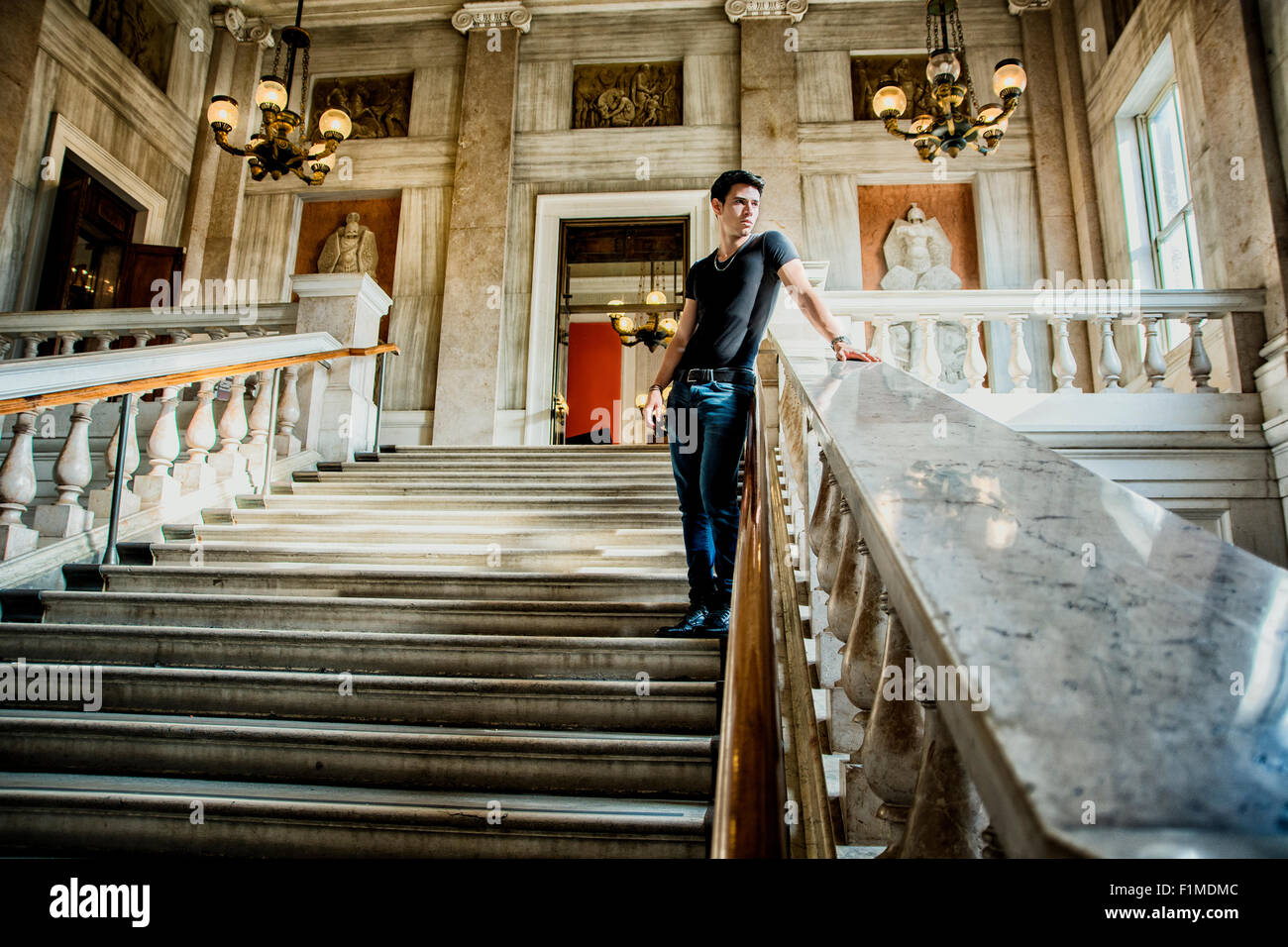 Giovane uomo bello in piedi sulle scale e appoggiata contro la rampa all'interno di un edificio architettonico mentre guardando in lontananza. Foto Stock