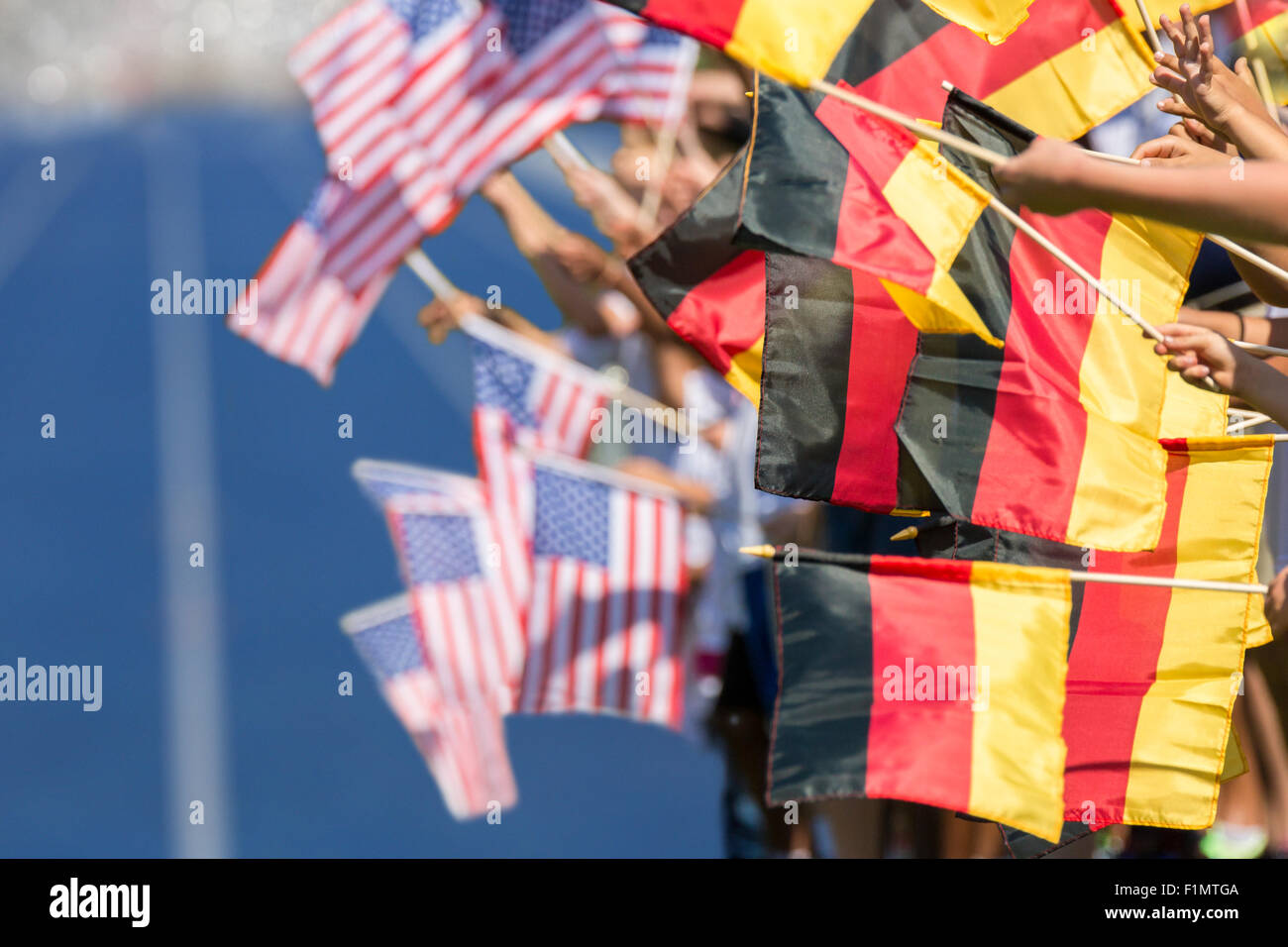Gli spettatori che ondeggia con bandiere di Germania e Stati Uniti di fronte ad un tartan blu via. Focus è il tedesco bandiere in primo piano Foto Stock