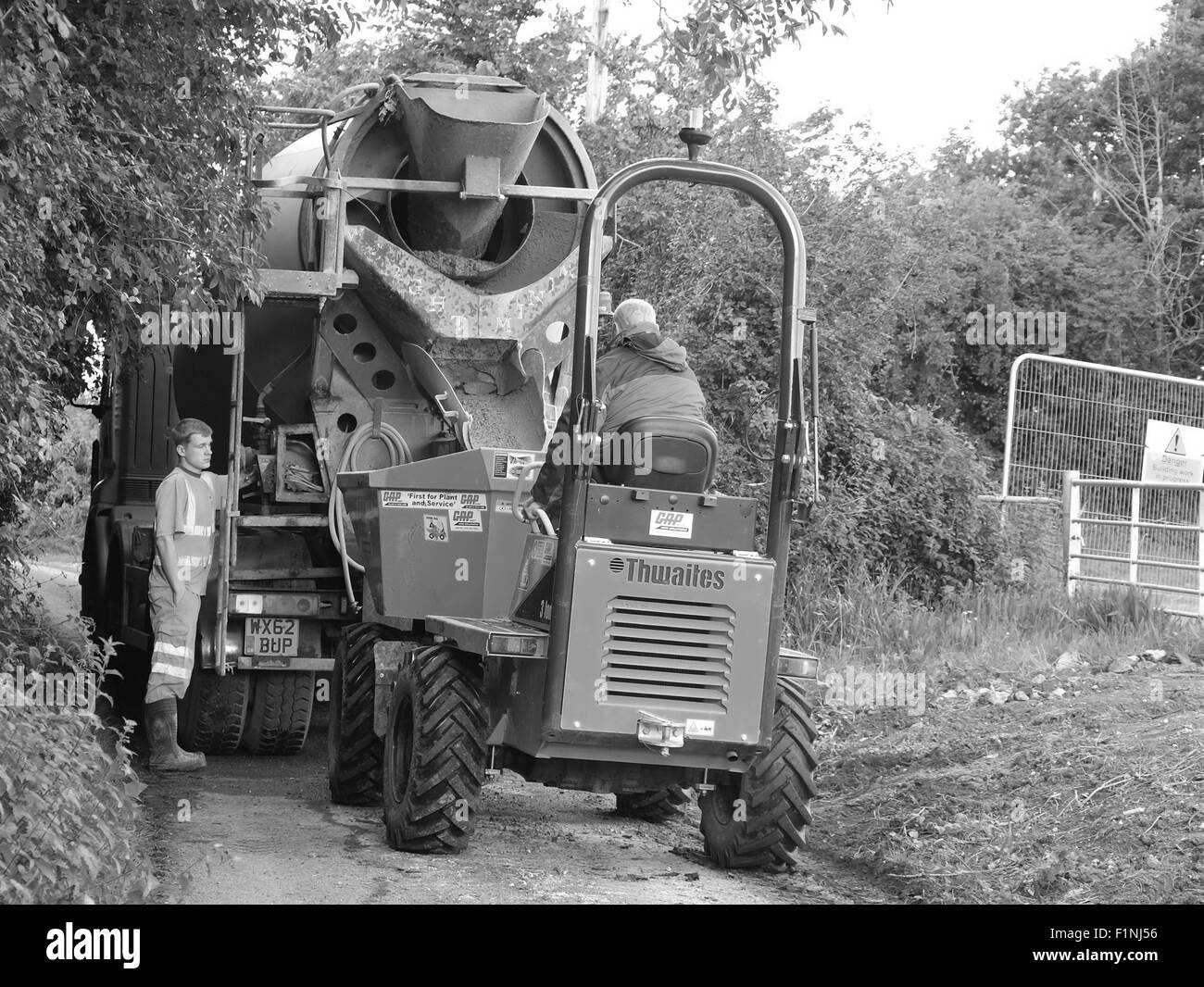 Lo scarico di un carrello di calcestruzzo in uno stretto vicolo del paese in un piccolo costruttori camion per la collocazione su una fattoria Foto Stock