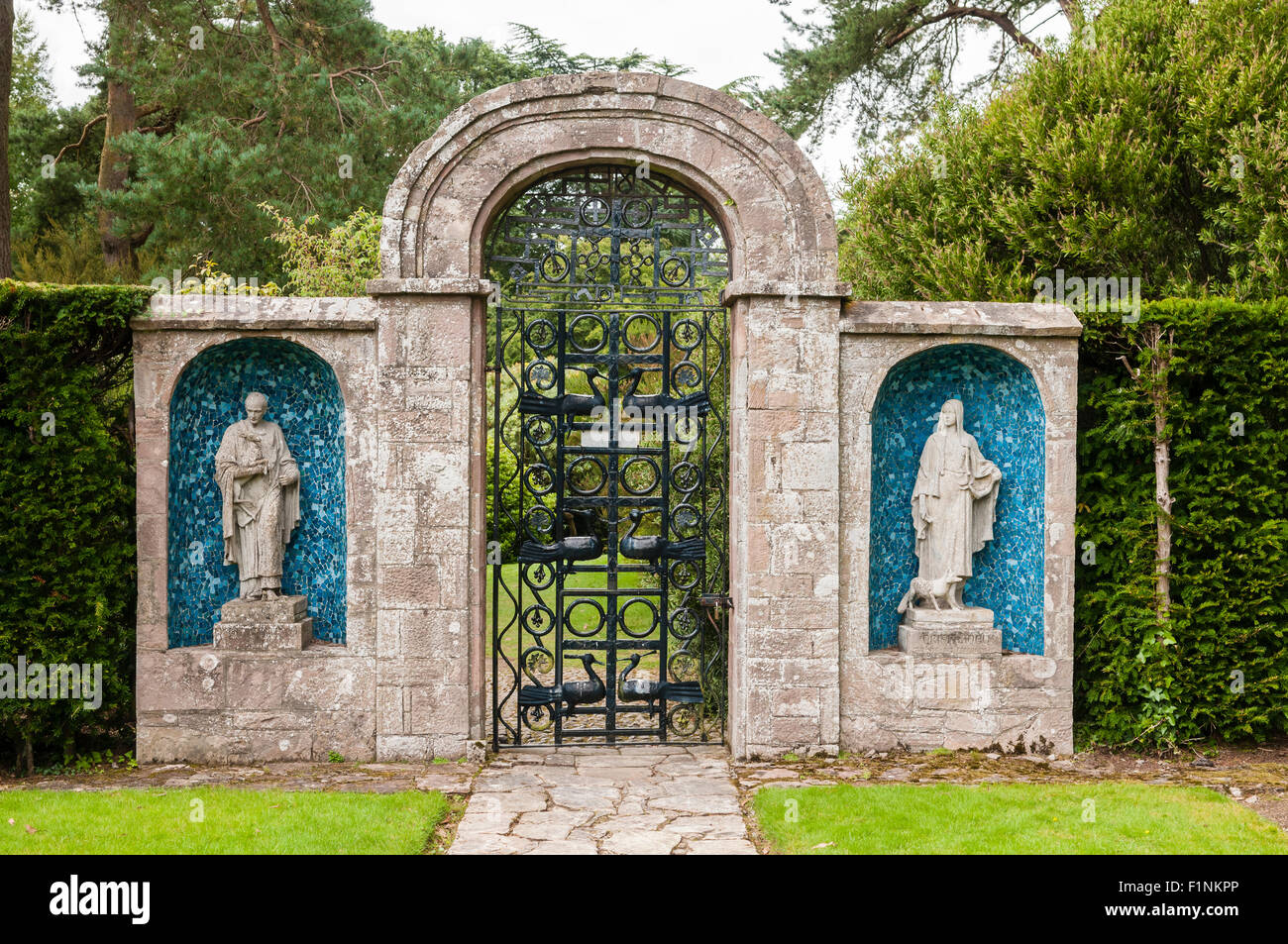 Due statue poste su entrambi i lati di una porta in acciaio e arco in pietra in un giardino formale Foto Stock