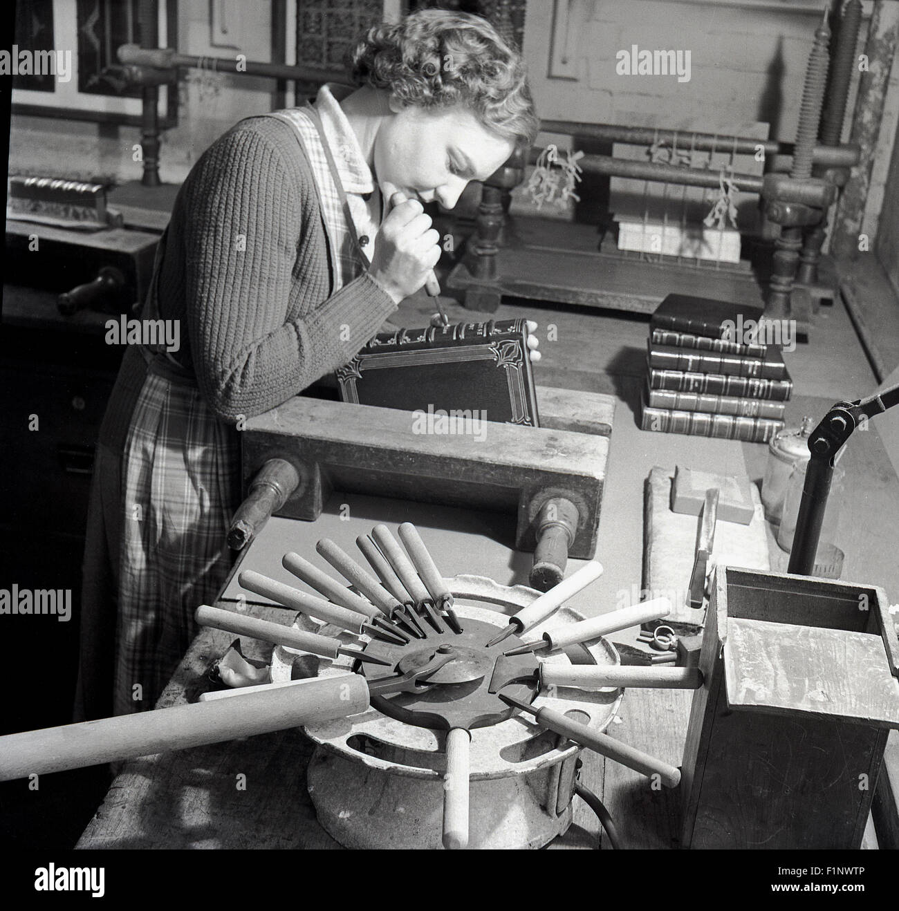 Storico degli anni cinquanta, lady in laboratorio utilizzando i metodi e gli strumenti tradizionali per tagliare , etch o incidere il dorso di un libro Foto Stock
