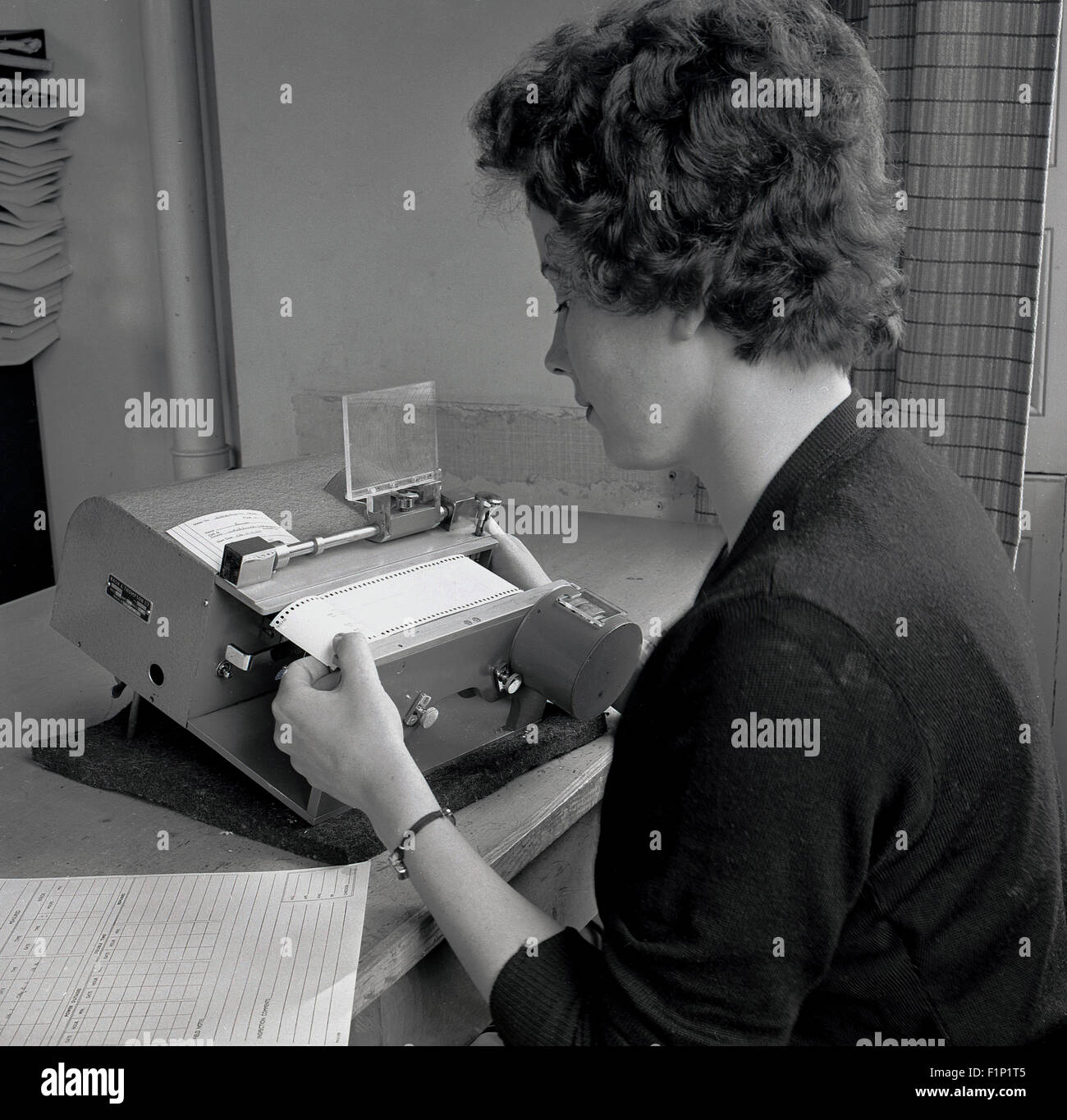 Storico degli anni cinquanta, la foto che mostra una donna segretario o account assistant o addetto al lavoro utilizzando una piccola macchina per la stampa. Foto Stock