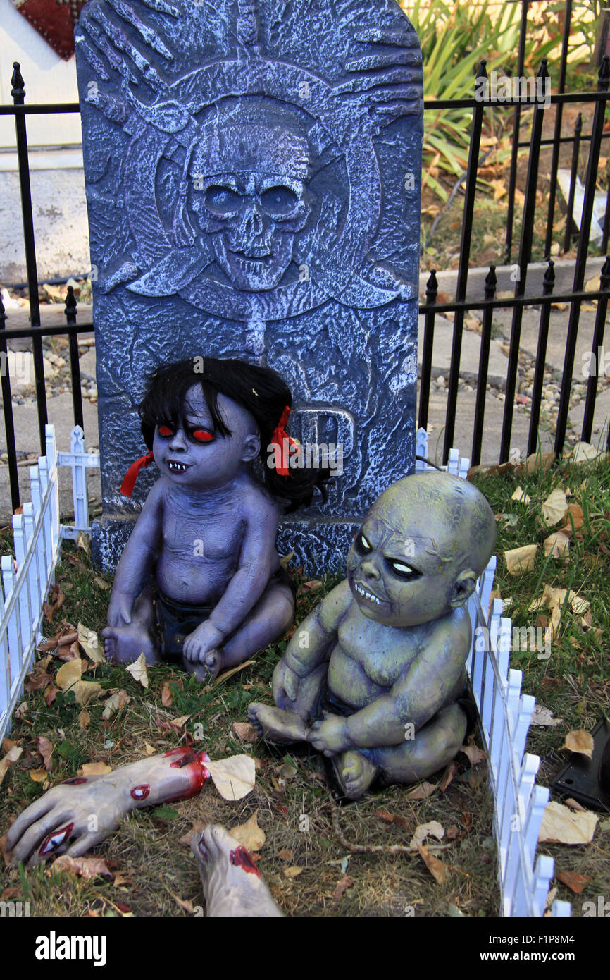 Creepy zombie baby dolls di sedersi di fronte una lastra tombale Foto Stock