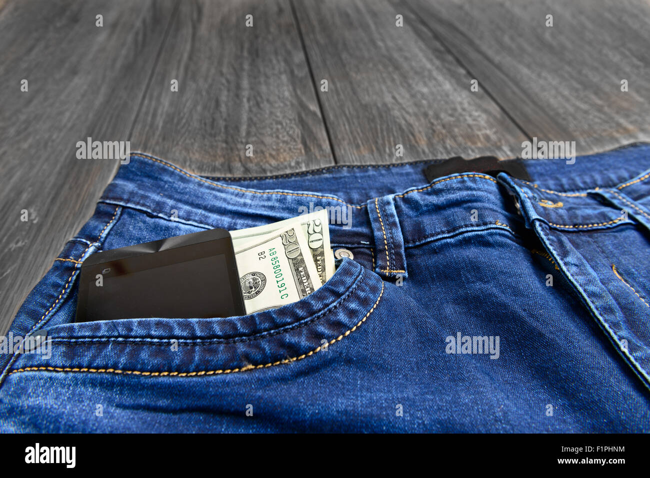 Jeans blu con il denaro e il telefono in tasca a sfondo di legno Foto Stock
