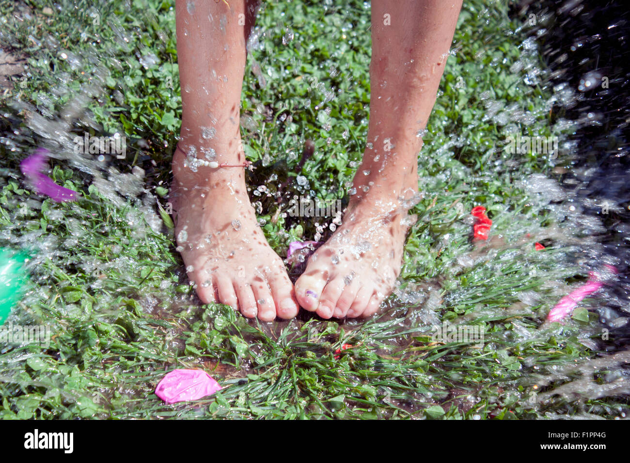 Una vista orizzontale di una spruzzata di un palloncino di acqua su una bambina piedi Foto Stock