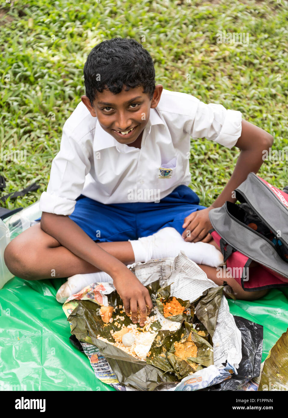 Scuola-boy a mangiare il pranzo al Reale Orto Botanico di Peradeniya vicino a Kandy, Sri Lanka Foto Stock
